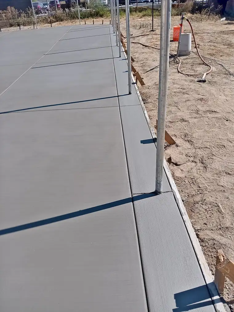 Freshly finished broom-textured concrete slab with curb edge and steel fence posts, forms still in place