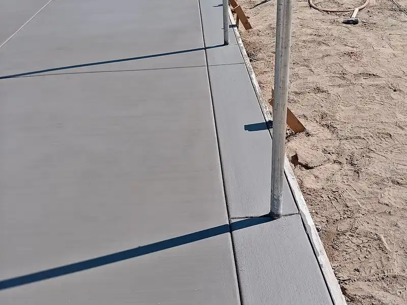 Freshly finished broom-textured concrete slab with curb edge and steel fence posts, forms still in place