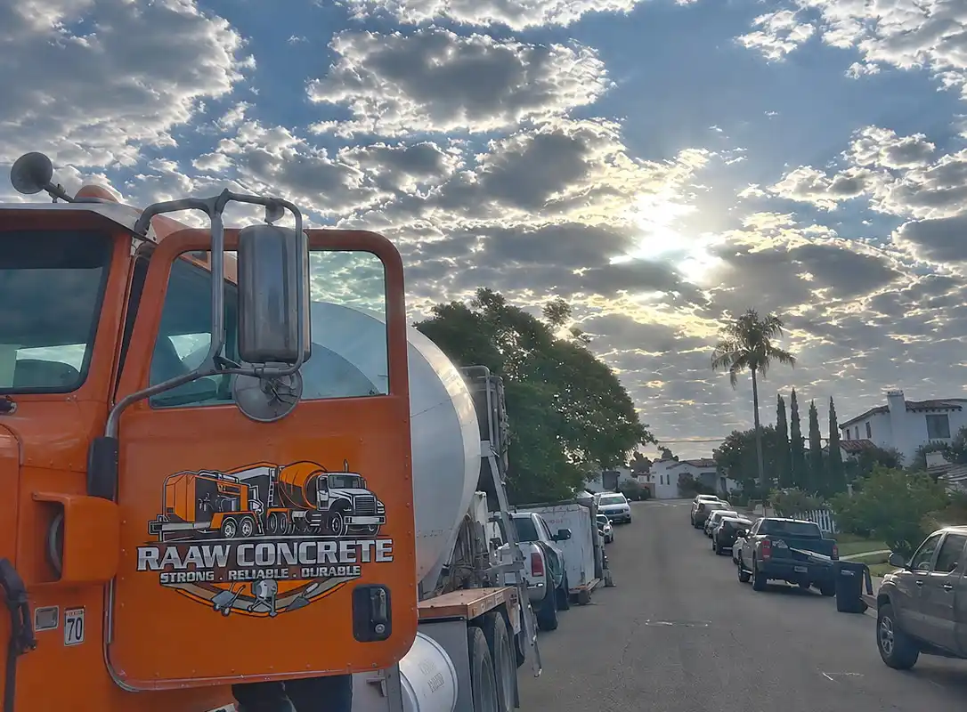 Orange Raaw Concrete Inc. mixer truck with branded cab door parked on a residential street under a dramatic cloudy sky