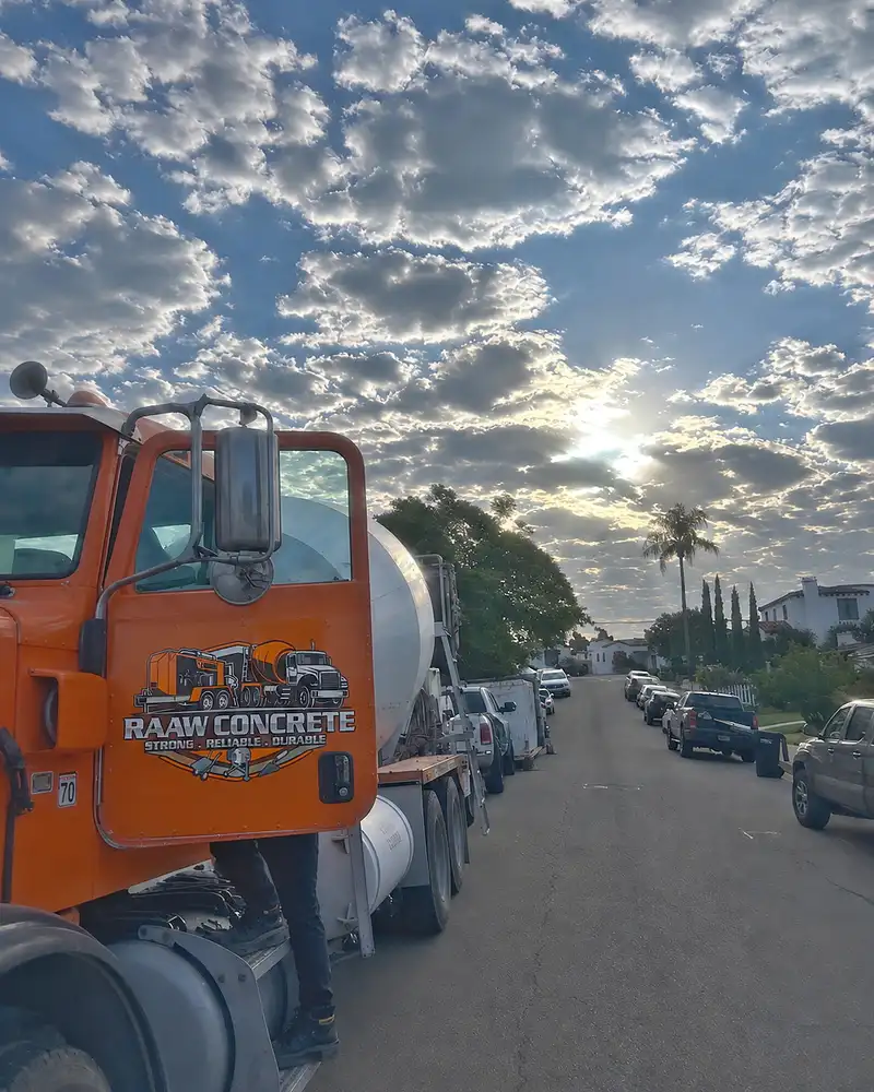 Orange Raaw Concrete Inc. mixer truck with branded cab door parked on a residential street under a dramatic cloudy sky