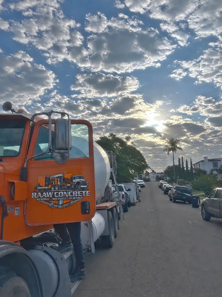 Orange Raaw Concrete Inc. mixer truck with branded cab door parked on a residential street under a dramatic cloudy sky