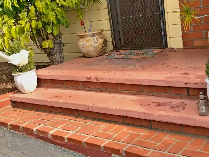 Worn front entry steps with peeling red paint over brick base