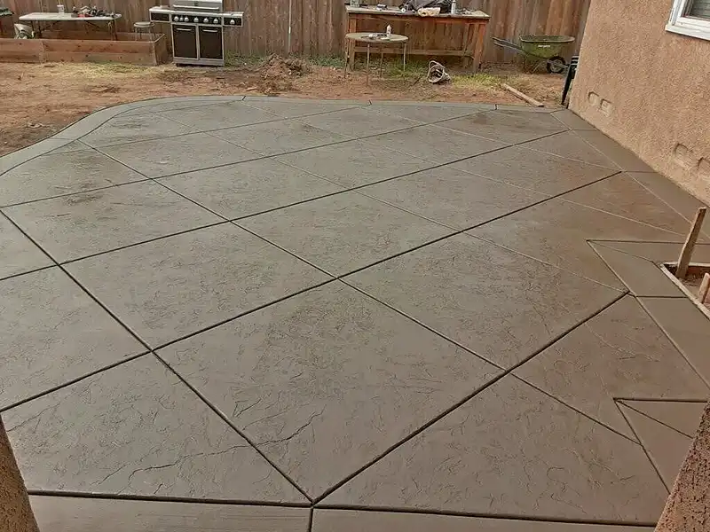 Stamped concrete patio with diamond-pattern slate texture and smooth border beside a stucco house in a backyard