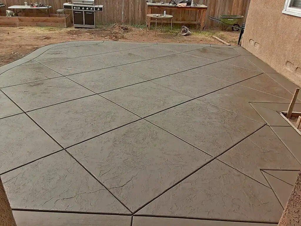 Stamped concrete patio with diamond-pattern slate texture and smooth border beside a stucco house in a backyard