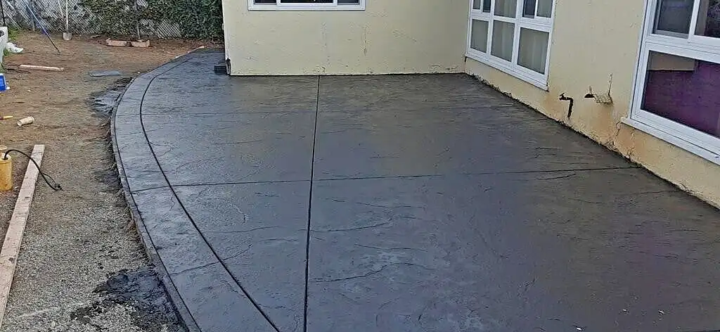 Dark charcoal stamped concrete patio with curved border behind a yellow stucco house