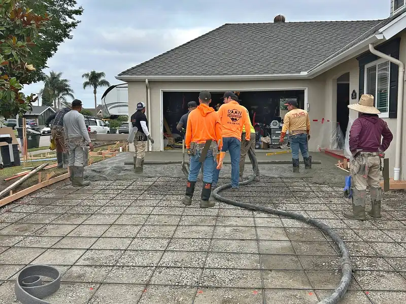 Raaw Concrete Inc. crew pumping concrete over a rebar grid for a residential driveway in front of a garage