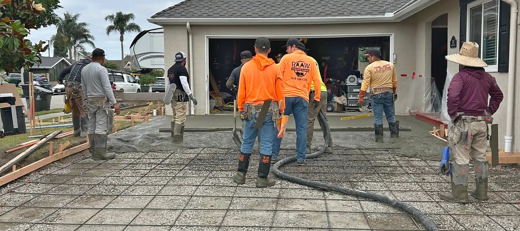Raaw Concrete Inc. crew pumping concrete over a rebar grid for a residential driveway in front of a garage