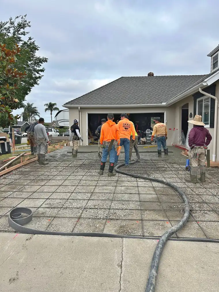 Raaw Concrete Inc. crew pumping concrete over a rebar grid for a residential driveway in front of a garage