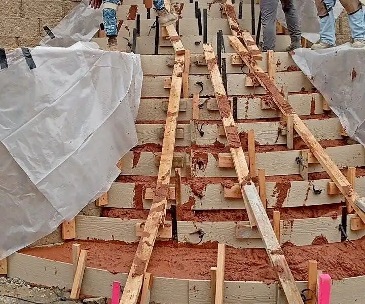 Crew pouring a curved concrete staircase through step forms between two block retaining walls