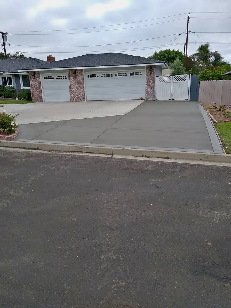 Freshly poured broom-finished concrete driveway extension beside a three-car garage, forms still in place