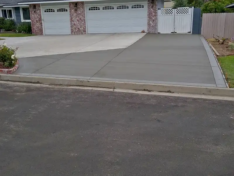Freshly poured broom-finished concrete driveway extension beside a three-car garage, forms still in place