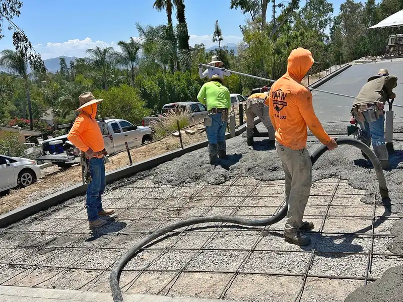 Raaw Concrete Inc. crew pumping and spreading concrete over rebar grid on sloped residential driveway