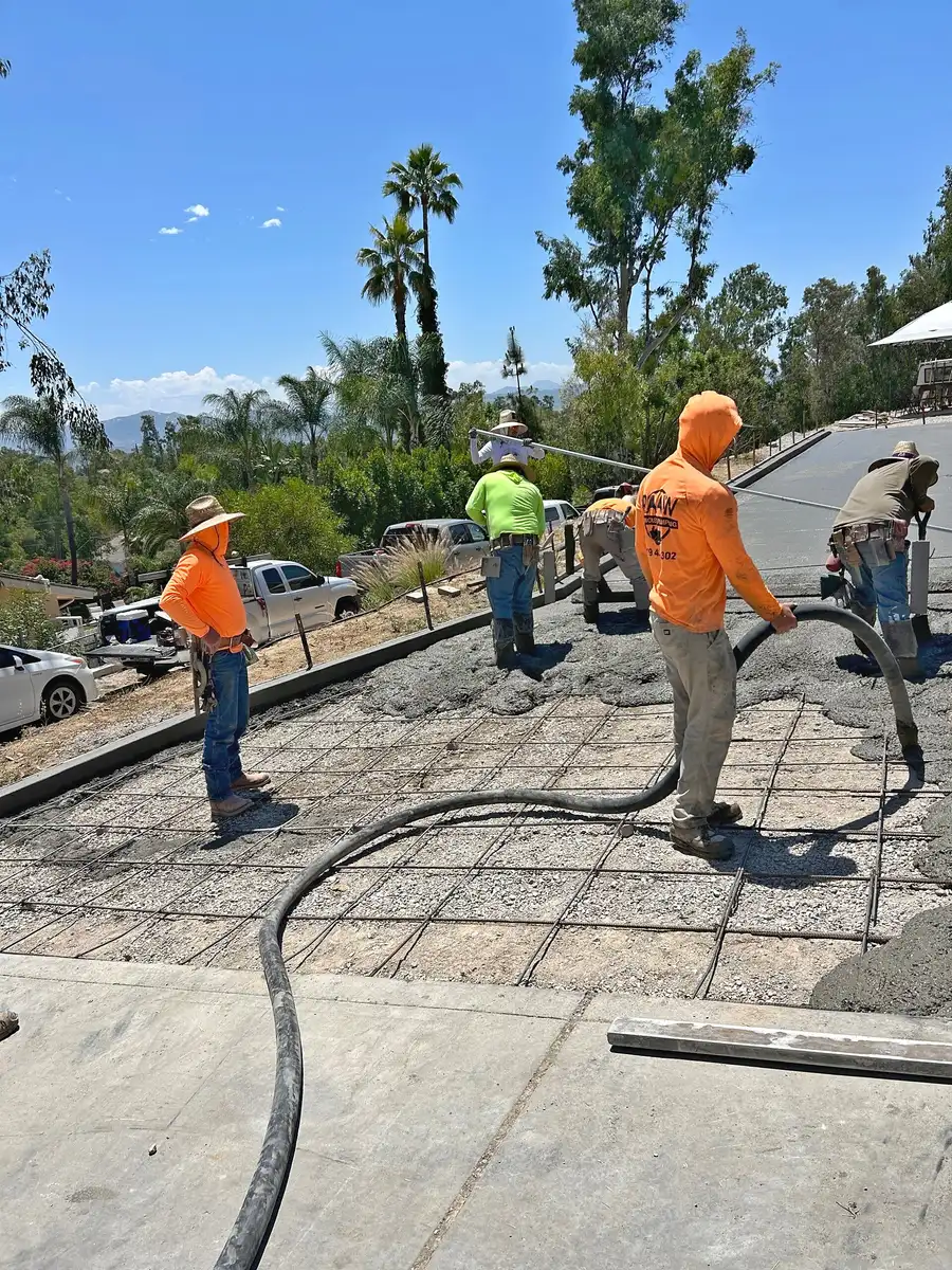 Raaw Concrete Inc. crew pumping and spreading concrete over rebar grid on sloped residential driveway