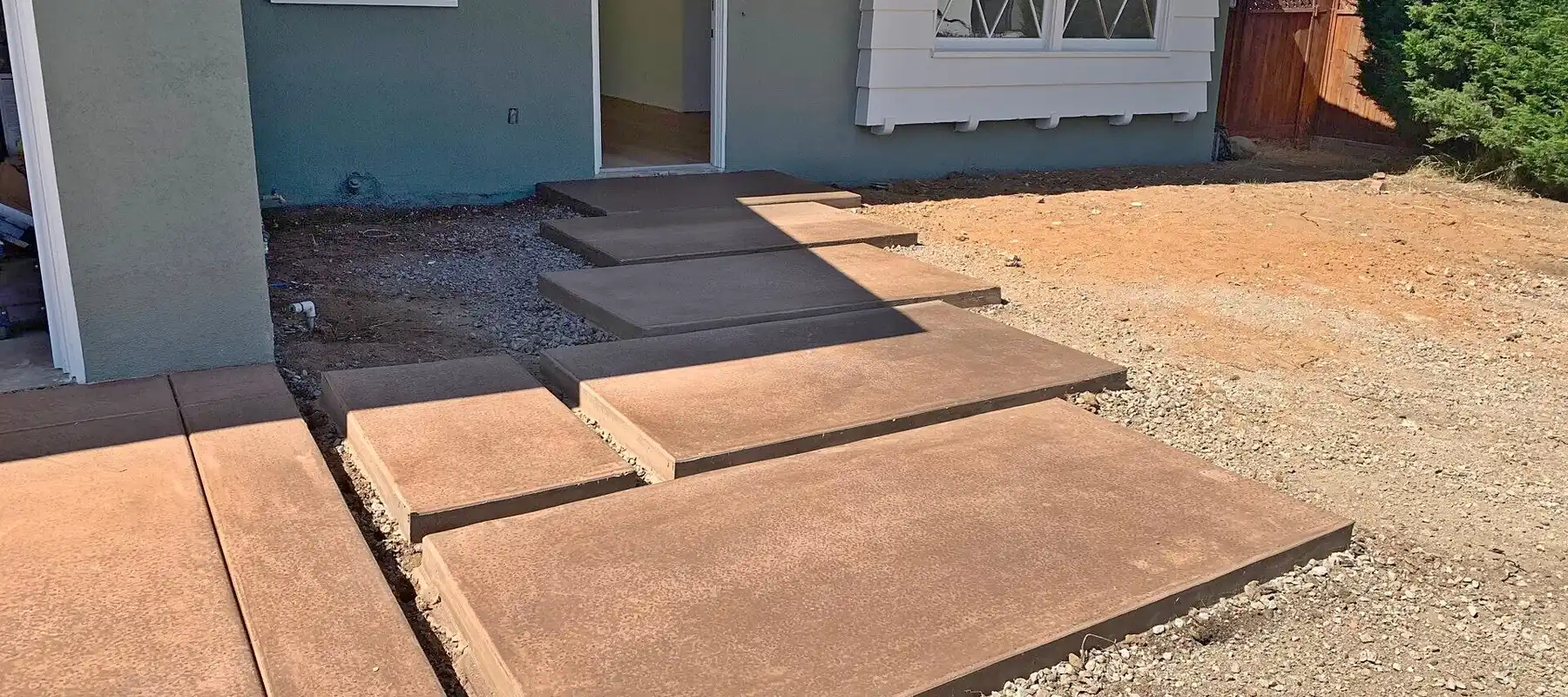 Colored concrete steps and landing pads leading to a home's back door, forms stripped, bare dirt around