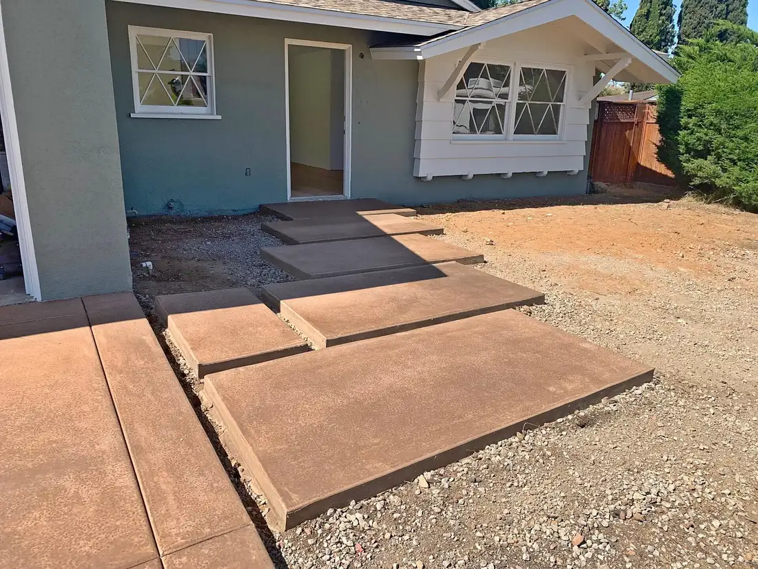 Colored concrete steps and landing pads leading to a home's back door, forms stripped, bare dirt around