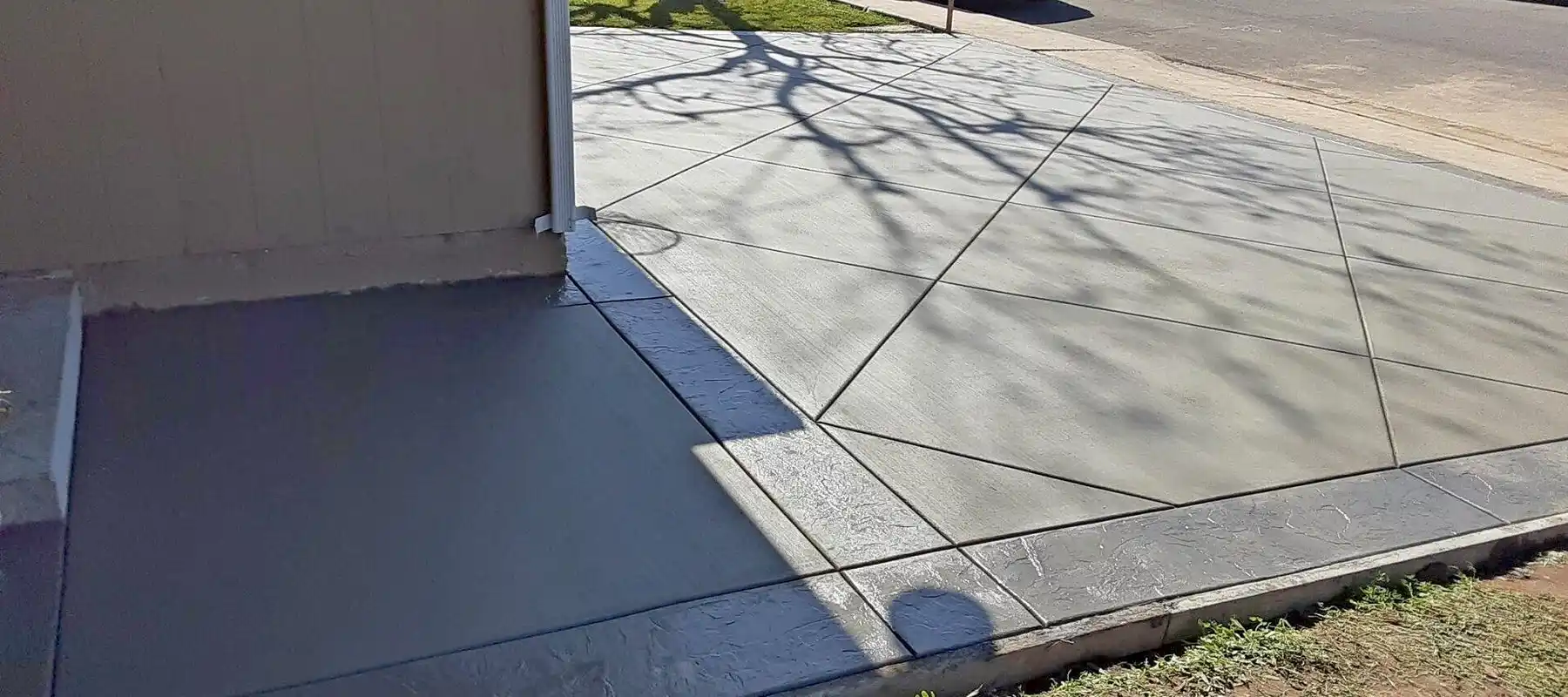 Freshly finished concrete driveway with diagonal control joints and dark textured border beside a garage