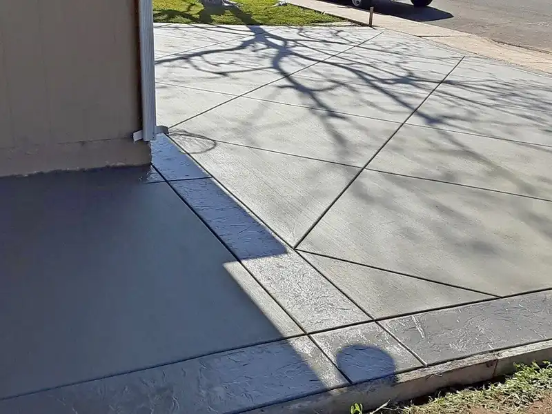 Freshly finished concrete driveway with diagonal control joints and dark textured border beside a garage