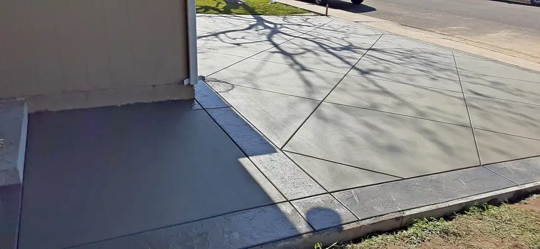 Freshly finished concrete driveway with diagonal control joints and dark textured border beside a garage